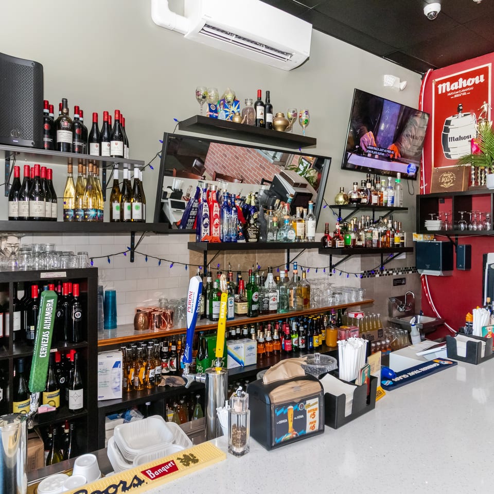 Fully stocked restaurant bar with wine and liquor bottles, beer taps, glassware, shelves, television, and colorful Malohu beer decor.