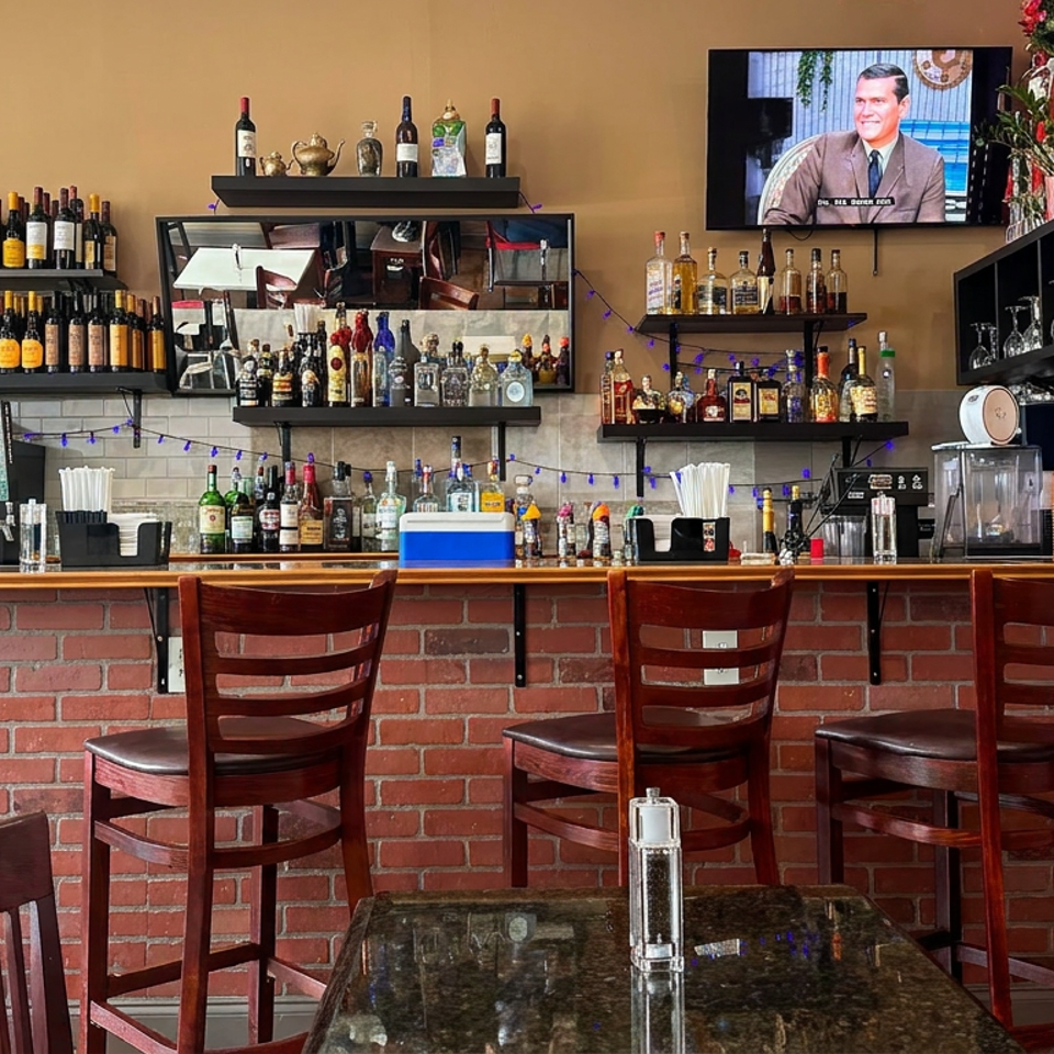 Restaurant bar with brick counter, wooden stools, liquor shelves, televisions, coffee equipment, and a staff member behind the counter.