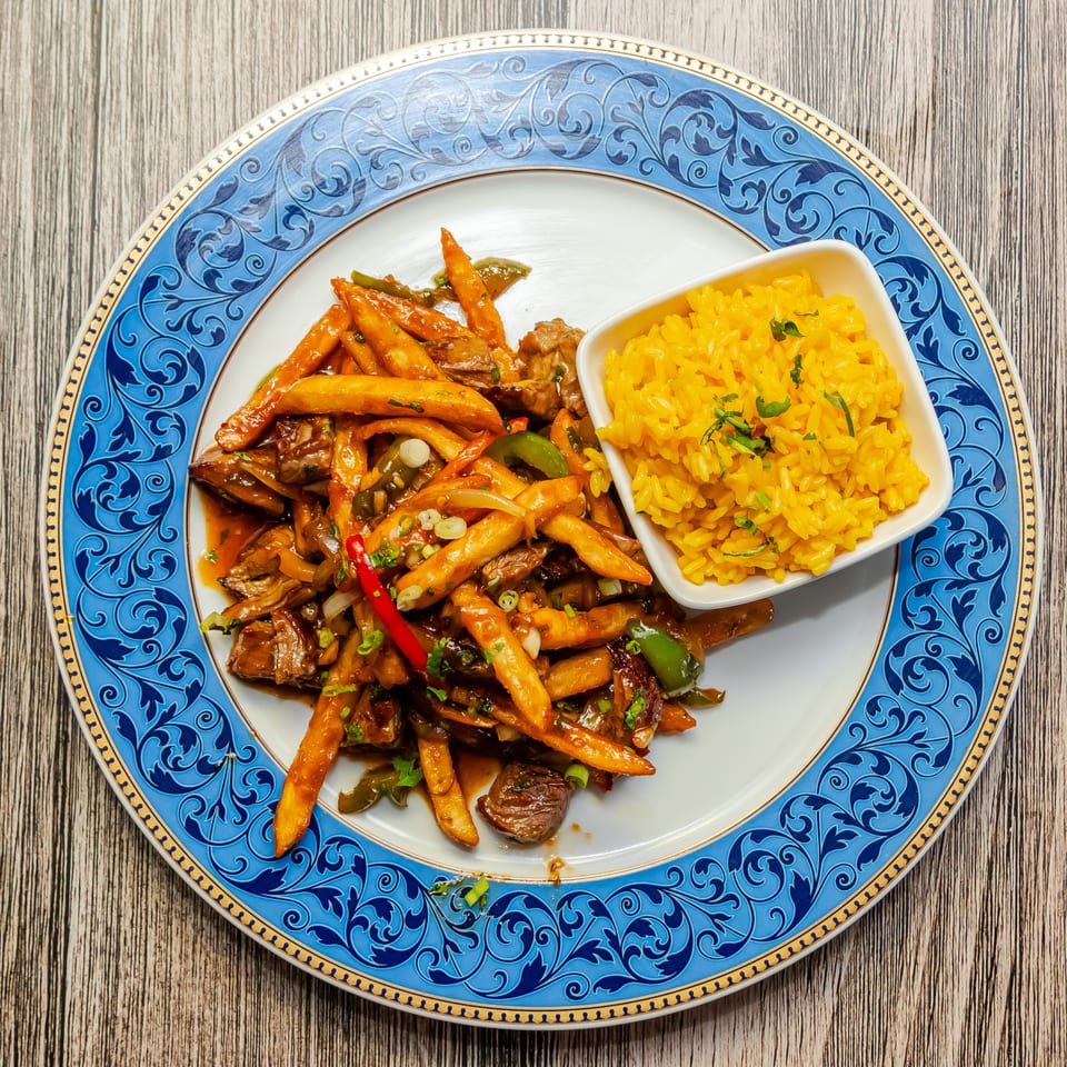 Sautéed beef and vegetables with golden fries and yellow rice on an ornate blue plate.