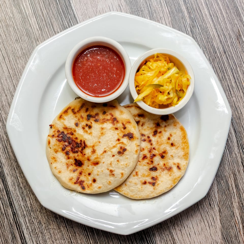 Grilled flatbreads served with red dipping sauce and shredded cabbage slaw on a white plate.
